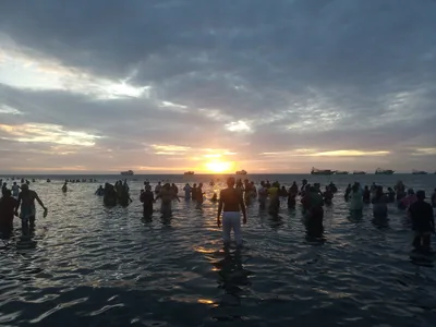 People standing in the sea at sunrise for a holy dip at Rameswaram, seen as dark shapes