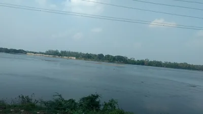 A wide full river under a blue sky with green trees along the far bank