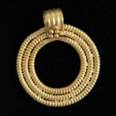A round gold pendant of coiled gold wire on a black background