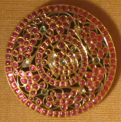 A round gold ornament set with rubies and emeralds in a flower pattern