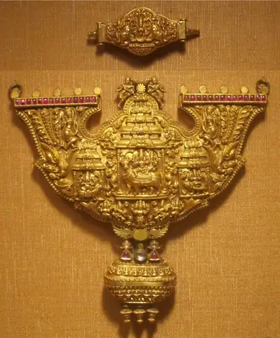 A large gold pendant with a carved temple scene in the centre