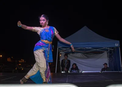 A dancer in a blue and gold costume performing on an open-air stage at night