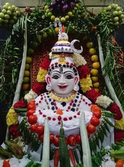 A Shiva lingam dressed with white rice, flowers and a face, framed by vegetables and fruit