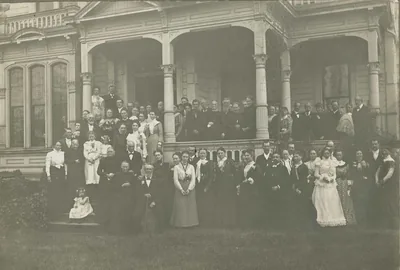 A large crowd of guests posing on the porch of a big house for a golden wedding anniversary