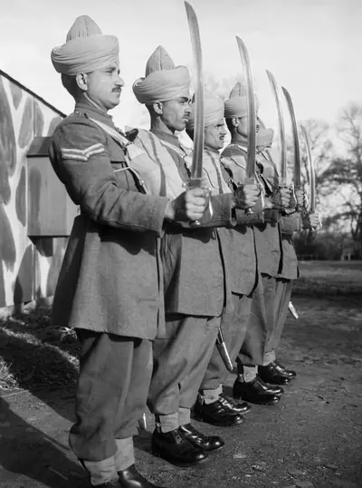 Black and white photo of Indian soldiers in turbans standing in a line holding drawn swords