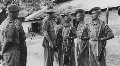 Black and white photo of a general inspecting a line of Indian soldiers in front of a hut