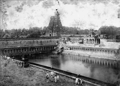 Old photo of a temple tank with a tower in the distance and people on the steps