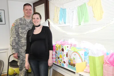 A couple standing by a table of wrapped gifts under a line of tiny baby clothes