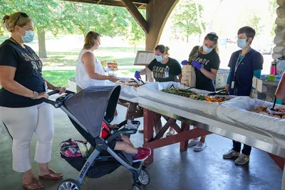 Guests at tables under a park shelter at a baby shower, with a pram nearby