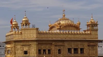 Close view of the golden domes and carved walls of the Golden Temple under a blue sky