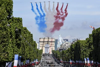 Jets trail blue, white and red smoke over a tree-lined avenue and the Arc de Triomphe