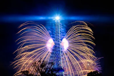 The Eiffel Tower lit in blue with fans of white fireworks on both sides