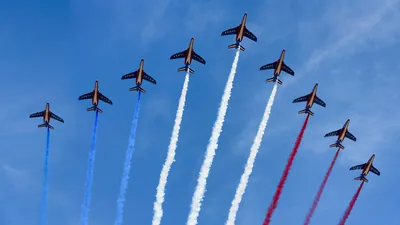 A line of jets in a blue sky trailing blue, white and red smoke