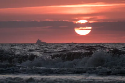 A red sun setting over rolling sea waves