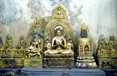 Old golden stone statues of the seated Buddha and Bodhisattvas against a weathered wall