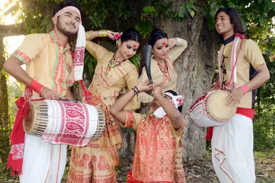 Young dancers in golden mekhela chador and men with dhol drums performing Bihu under a tree