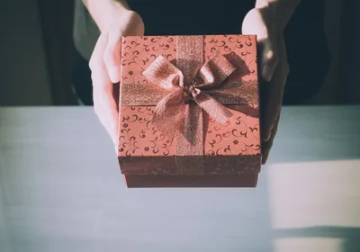 Hands holding out a brown gift box with a bow