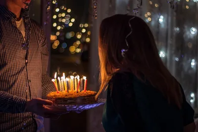A cake with lit candles carried towards a person in a dim room with fairy lights