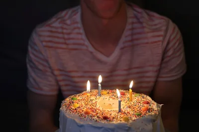 A round cake with sprinkles and lit candles held in front of a person