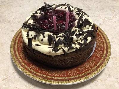 A chocolate and cream cake with cherry topping and pink candles on a plate