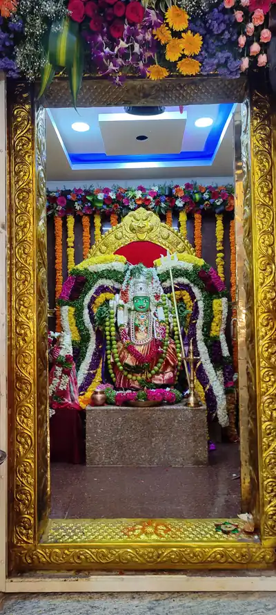 A goddess idol covered in white and red flower garlands inside a shrine with a golden frame
