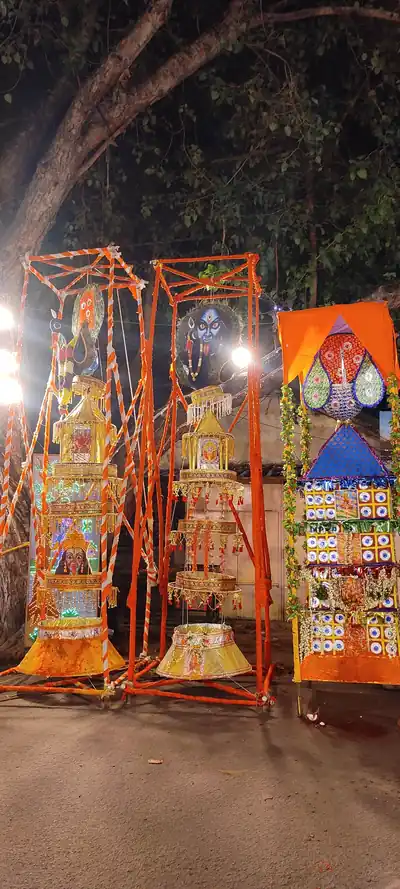 Tall decorated frames of coloured paper and cloth lit up in front of a temple at night