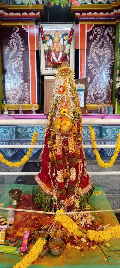A tall red and gold decorated offering covered in marigolds in front of a temple