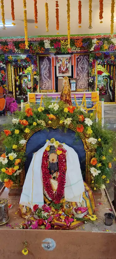 A shrine of the goddess draped in white with orange and yellow flower garlands around an arch
