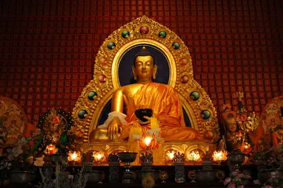 A golden Buddha statue in a richly decorated shrine with small lamps