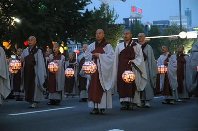 Buddhist monks in robes walk in a line carrying round paper lanterns
