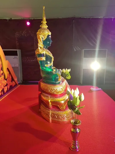 A green Buddha statue on a golden throne with lotus flowers in front