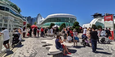 A crowd in red and white walks past a glass building on a sunny day