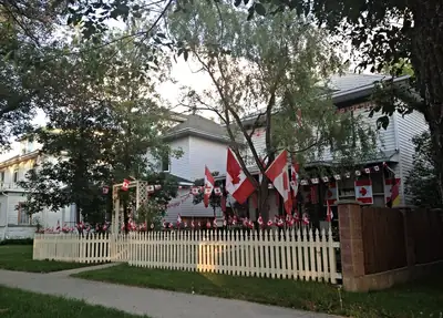 A house with a white picket fence decorated with many red and white maple leaf flags