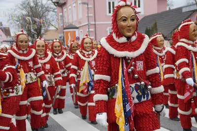 A line of people in red costumes and carved wooden masks marching