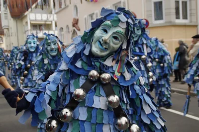 Marchers covered in blue and green fabric scraps with masks and bells
