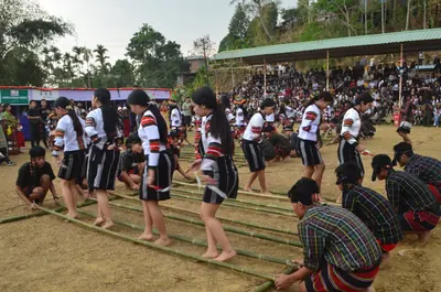 Women in black and white striped puan stepping between bamboo poles held by kneeling men before a large crowd