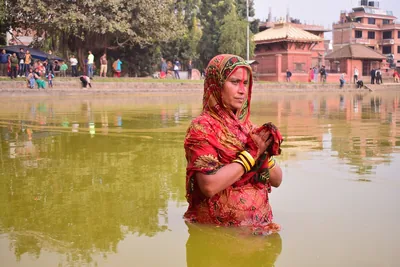 A devotee in a red sari stands waist-deep in a temple pond with folded hands