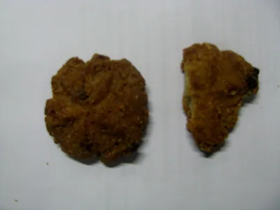 Two golden brown thekua biscuits on a white surface