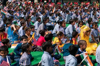 A large group of school students in uniform sitting on a green floor and waving small flags