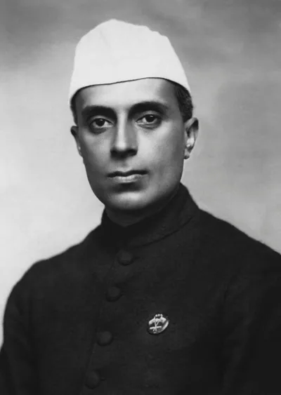 Black and white portrait of a young Jawaharlal Nehru in a dark coat and white cap