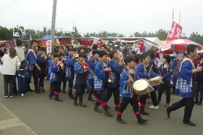 A school band in blue uniforms marching with drums along a festival street