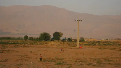 Kites flying in the sky over a dry field at the foot of mountains