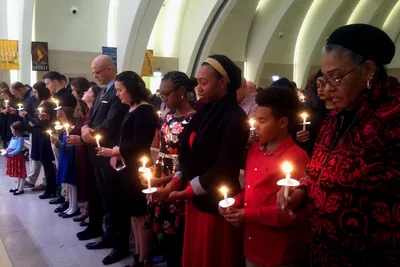 A congregation stands holding small lit candles