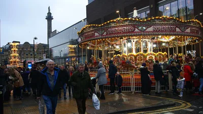 People walk past a bright carousel at a Christmas fair