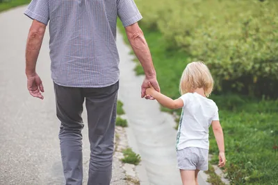 An older man holding a little girl's hand as they walk down a garden path