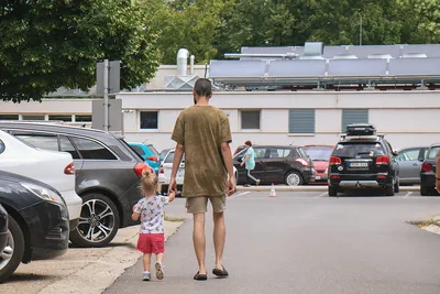 A father and his small daughter walking across a car park towards a building