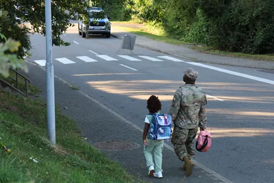 A father in uniform walking his daughter to school along a road on the first day of term