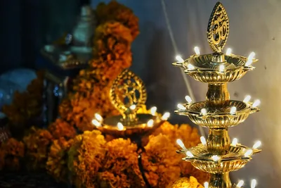 Brass lamps with many small flames beside marigold garlands