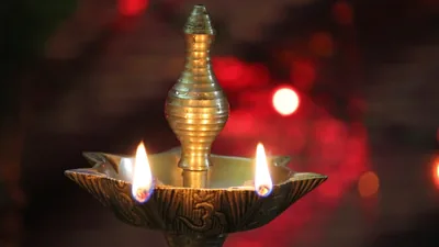 A tall brass oil lamp with two flames against a red background