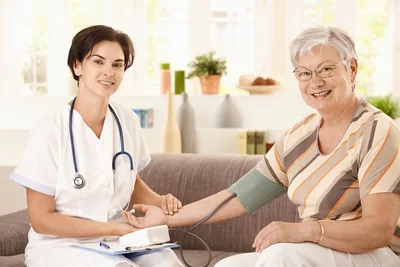 A smiling health worker checking an older woman's blood pressure at home